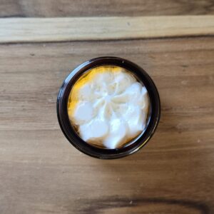 An amber jar with no lid, filled with whipped tallow sitting on a wood surface